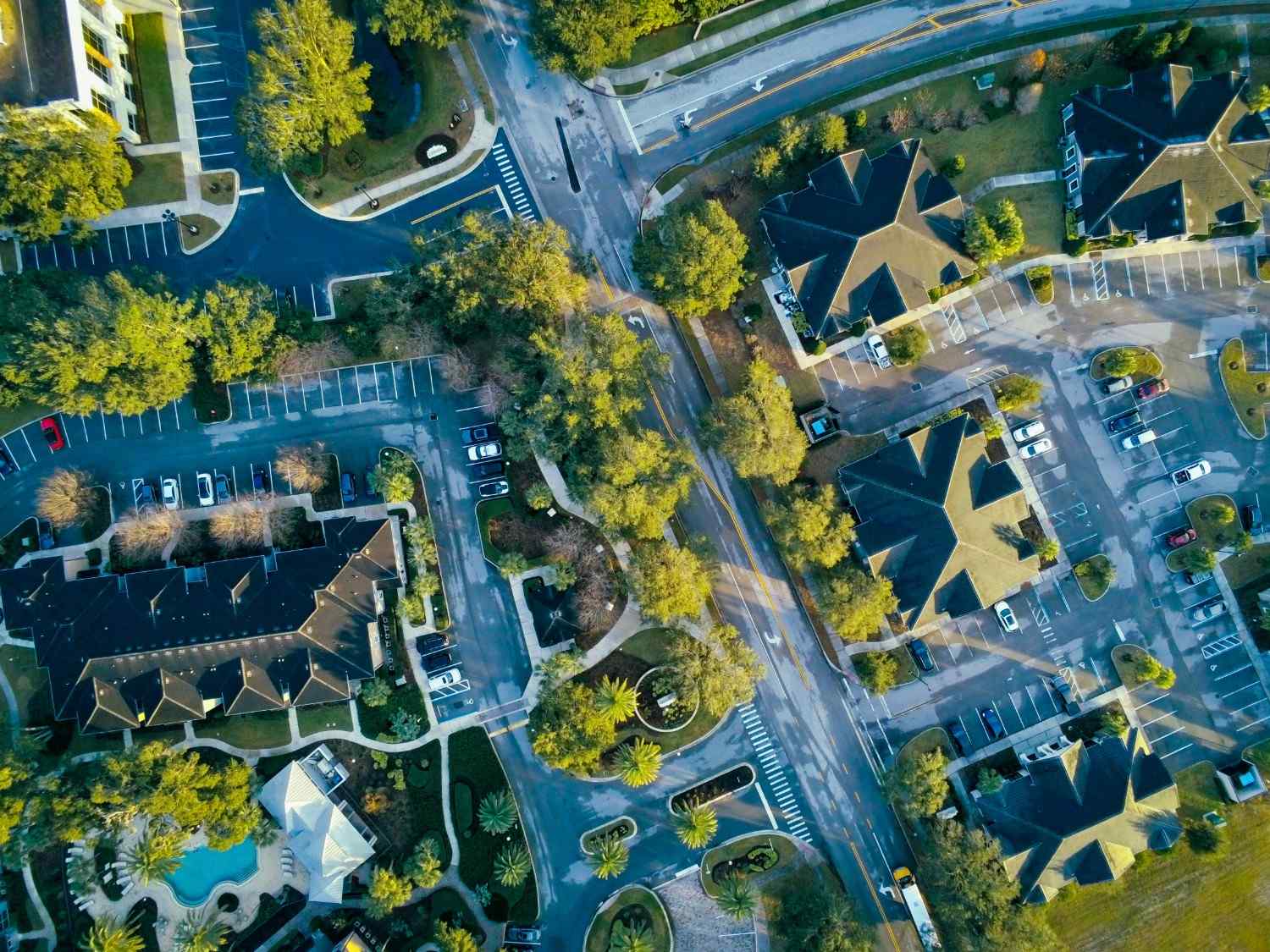 An aerial, top-down view of a master-planned community managed by WRMC, showing multi-family residential complexes, tree-lined streets, parking structures, and a swimming pool facility.