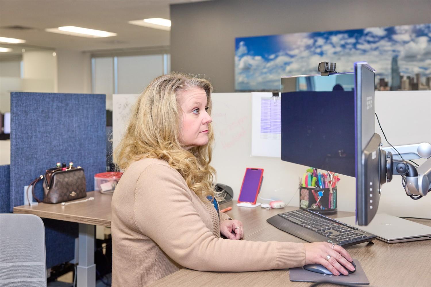Profile view of a blonde female WRMC employee working diligently on a dual-monitor desktop setup in a modern open office.