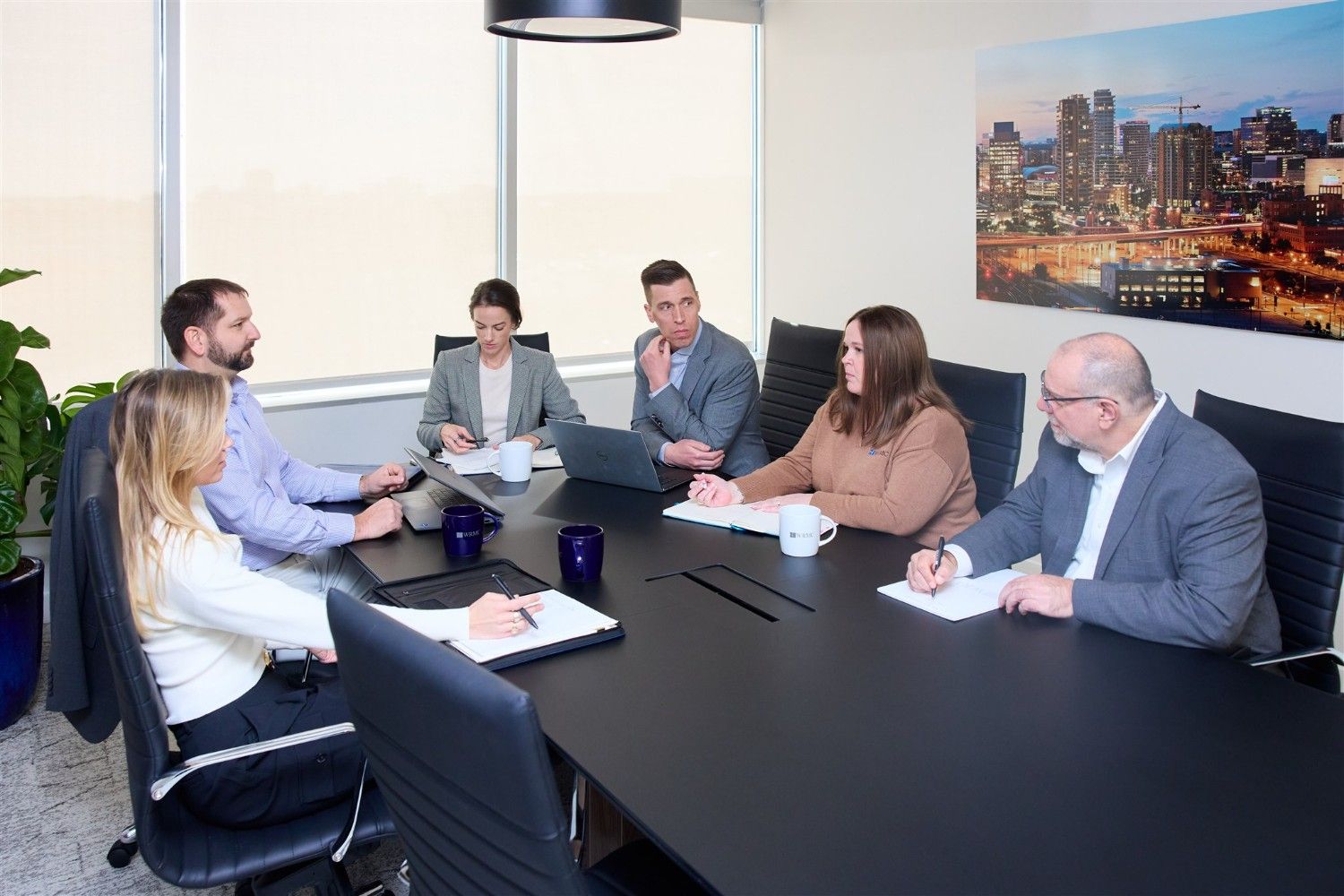 A diverse group of six WRMC corporate executives holding a strategic planning meeting around a large black boardroom table.