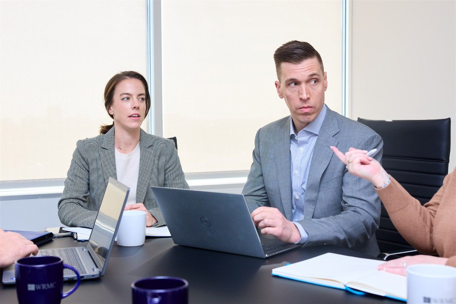 A close-up of a female and male WRMC executive listening intently during a collaborative team meeting with laptops open.
