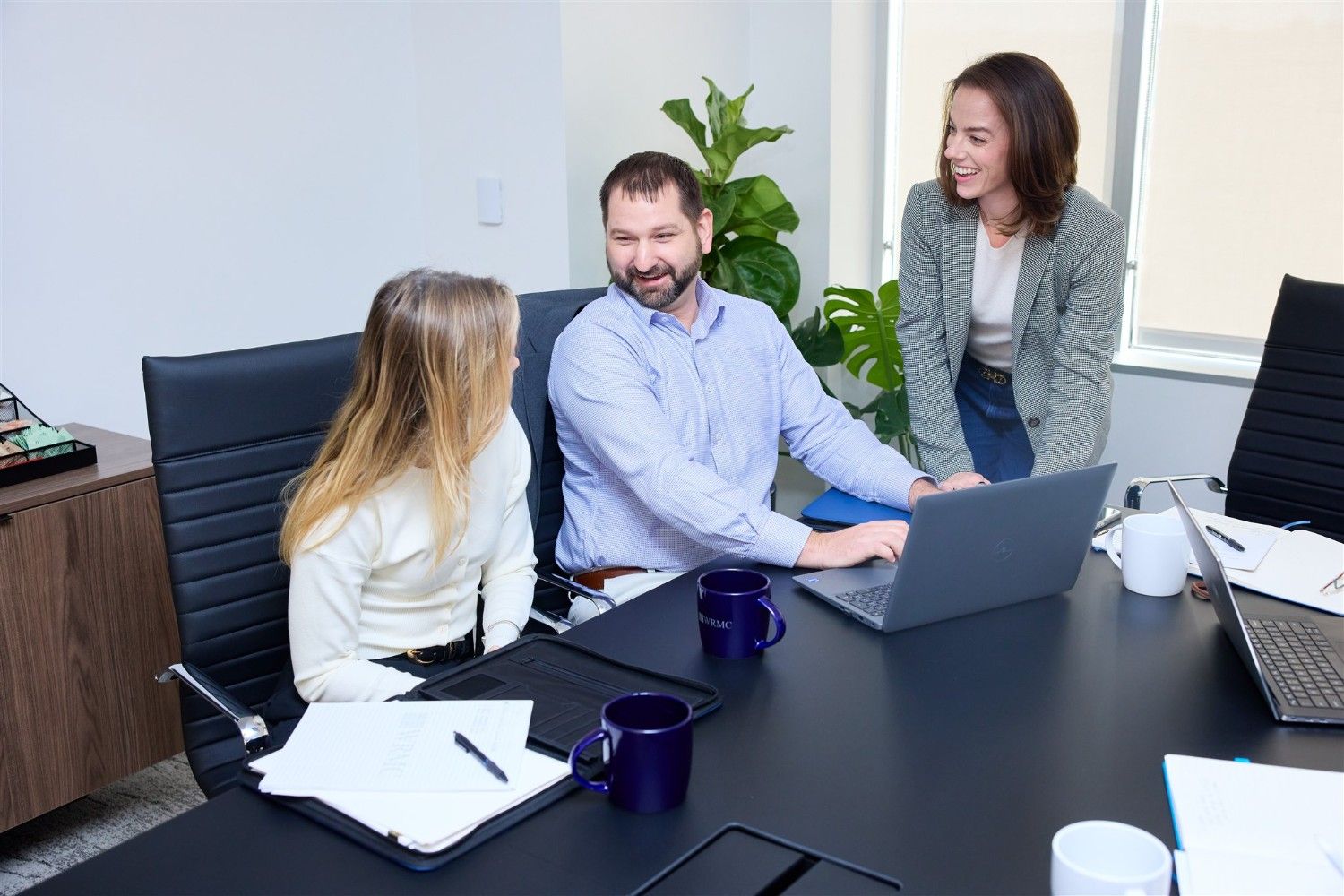 Three WRMC colleagues smiling and collaborating around a laptop computer at a conference room table.