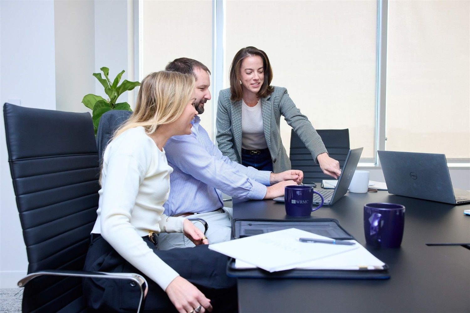 A female WRMC manager points to a laptop screen to guide two colleagues sitting at a conference table.